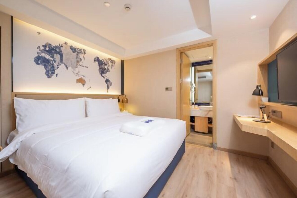 Ein modernes Hotelzimmer mit einem großen Bett, einer Weltkarte an der Wand, einem Schreibtisch mit Lampe und einem Spiegel.