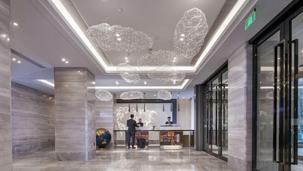 Un hall d’hôtel moderne doté d’un comptoir d’accueil, d’un sol en marbre et d’un éclairage au plafond original.