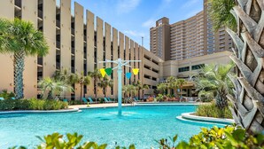 Un hotel con piscina, palmeras y un edificio alto al fondo.