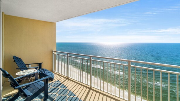 Un balcón con dos sillas Adirondack y una mesita redonda, con vista a la playa y al océano.