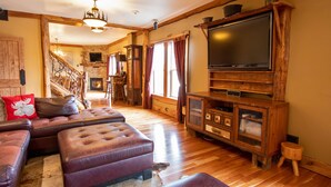 Una sala de estar acogedora con televisor grande, sofás de cuero, chimenea y una escalera rústica.