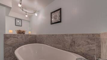 A modern bathroom with a freestanding bathtub, marble tiles, a chandelier, and framed artwork on the wall.