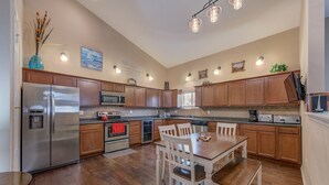 A modern kitchen with wooden cabinets, stainless steel appliances, and a dining area with white chairs. - Luxury 4BR Near Lake Pepin with Game Room - Breeze (Pepin)