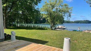 En træterrasse med et hvidt, cylinderformet objekt, et græsområde og en sø med både i baggrunden.