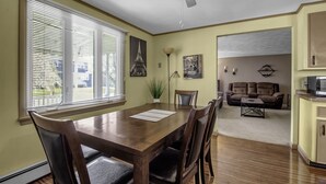 A dining area with a wooden table and chairs, a ceiling fan, and a view of a living room with a couch and a TV. - Quiet suburban home 10 minutes from airport/25 min from Niagara Falls (Depew)