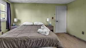 A neatly made bed with a brown comforter, two white pillows, and rolled towels on a nightstand. There is a window with purple curtains, a white door, and a ceiling fan. - Quiet suburban home 10 minutes from airport/25 min from Niagara Falls (Depew)