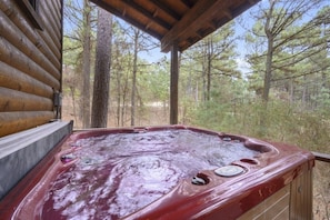 Un jacuzzi con revestimiento de madera, rodeado de un área boscosa.
