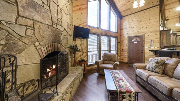 A cozy cabin interior with a stone fireplace, leather furniture, and a large window.