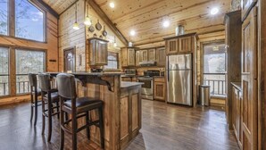 A spacious kitchen with wooden cabinets, a central island with bar stools, stainless steel appliances, and large windows.