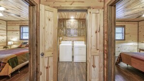 A log cabin interior with two bedrooms, a shared bathroom with a washing machine, and a central window.