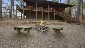 A wooden cabin with a deck and a fire pit in front.