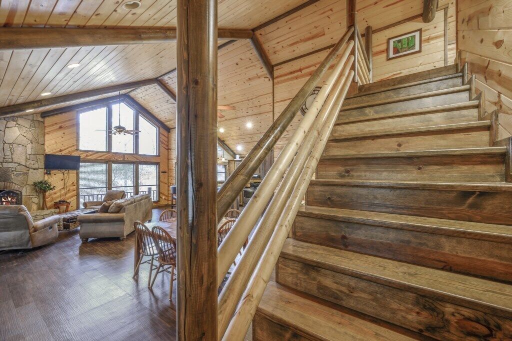 Eine Holztreppe führt zu einer Erkerwohnung mit Kamin aus Stein und großen Fenstern.