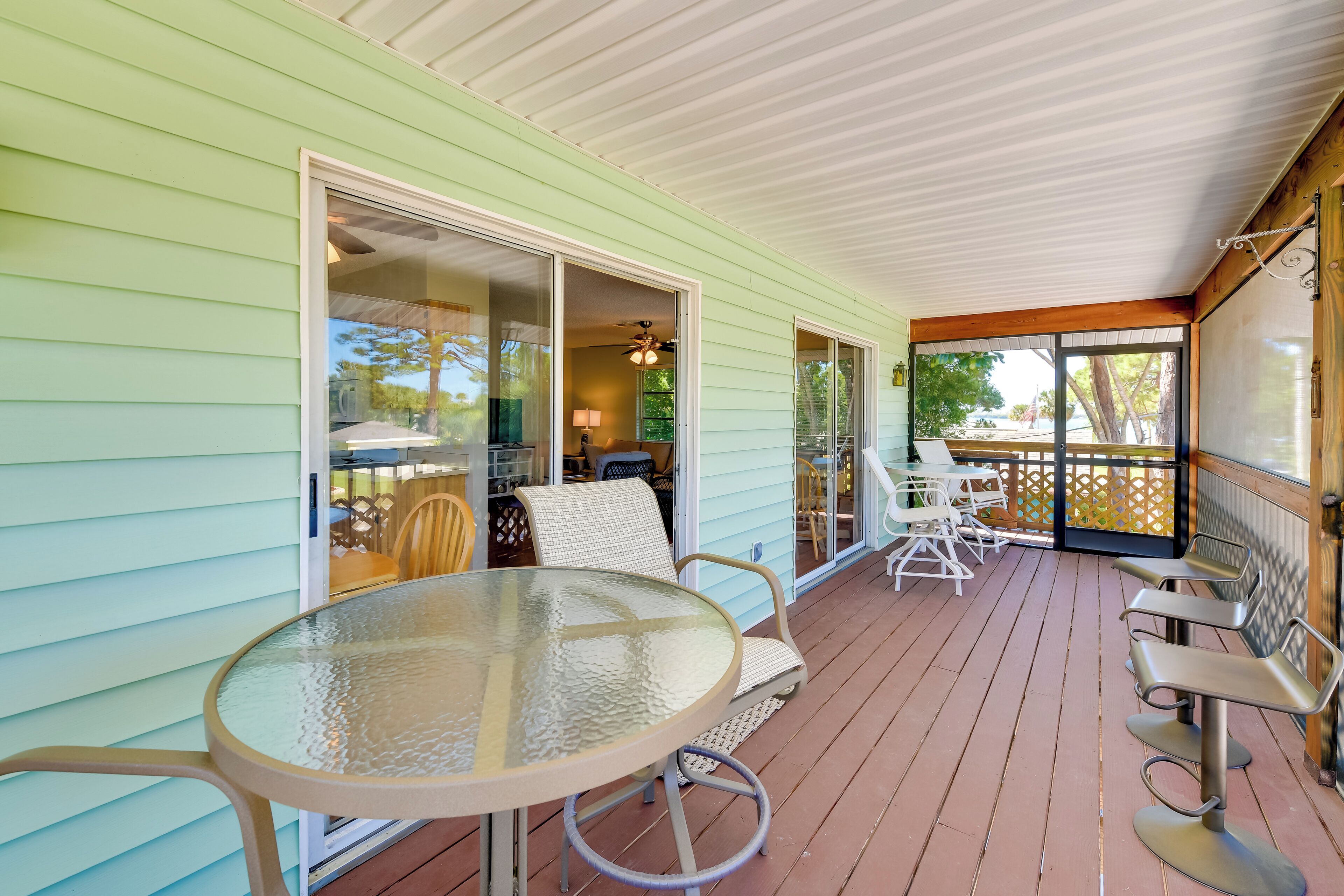 A covered porch with a glass table and chairs, a sliding glass door leading to an interior room, and a view of the outdoors.