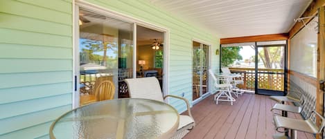 A covered porch with a glass table and chairs, a sliding glass door leading to an interior room, and a view of the outdoors.