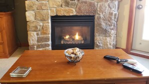 A stone fireplace with a fire, a wooden mantel, and a table with a glass bowl and remotes. - Ski-in / Ski-out best Solitude Resort Village Location (Cottonwood Heights)