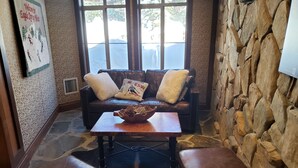 A cozy living room with a stone wall, a leather sofa with cushions, a wooden coffee table with a bowl, and leather ottomans. - Ski-in / Ski-out best Solitude Resort Village Location (Cottonwood Heights)