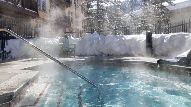 A hot tub surrounded by snow-covered trees and a building with balconies. - Ski-in / Ski-out best Solitude Resort Village Location (Cottonwood Heights)
