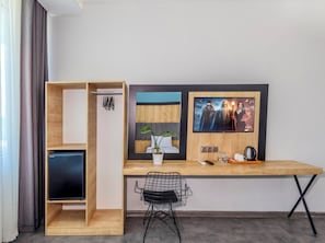 Moderni huone, jossa on puinen työpöytä, tuoli, televisio, viherkasvi ja sängyssä pääty.