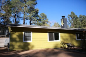 Set amidst tall pine trees, this charming home features a single-story design with a cozy porch and a classic chimney.