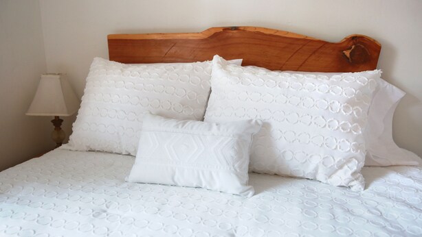 A neatly made bed with a wooden headboard, white bedding, and a bedside lamp. - Everything Evergreen (Prescott)