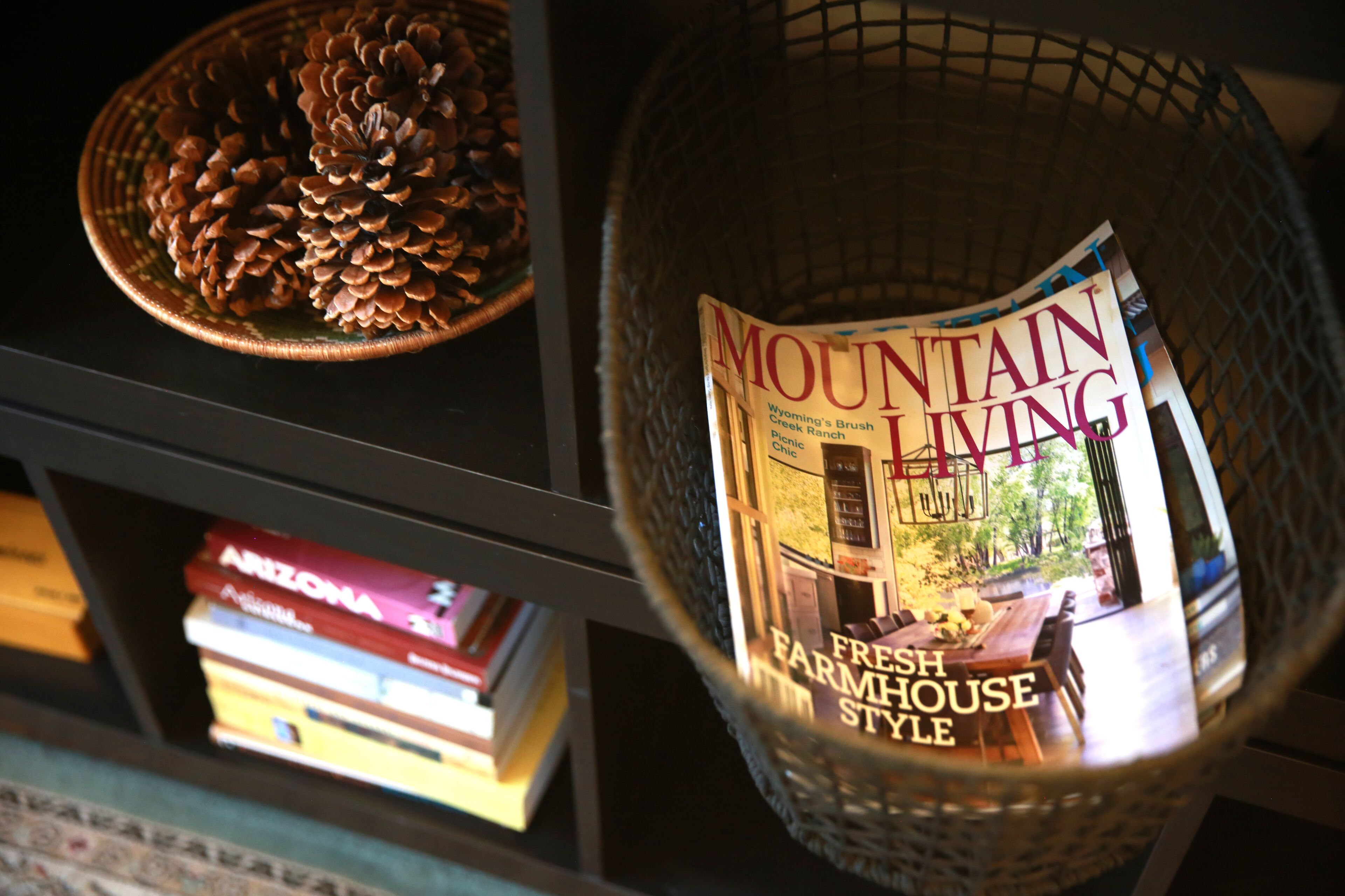 Una revista titulada 'Mountain Living' con una portada que dice 'Fresh Farmhouse Style', un piñón y libros en una estantería.