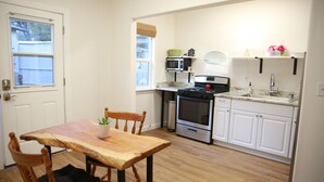 A compact kitchen with a wooden dining table, chairs, a microwave, oven, and white cabinets. - Everything Evergreen (Prescott)