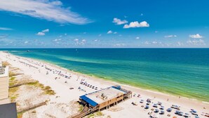 A beach with a long stretch of sand, a pier, and a building with a blue roof.