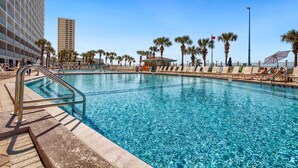 A swimming pool with clear blue water, surrounded by palm trees and a building with balconies.