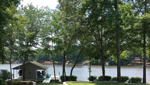 A lakeside property with a small dock, a covered seating area, and a grassy lawn.