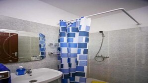 Een badkamer met een witte wastafel, een spiegel, een douche met een blauw-wit gestreept gordijn en een handgreep.