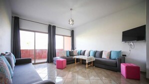 Een moderne woonkamer met een grote bank, een salontafel en een aan de muur bevestigde televisie.