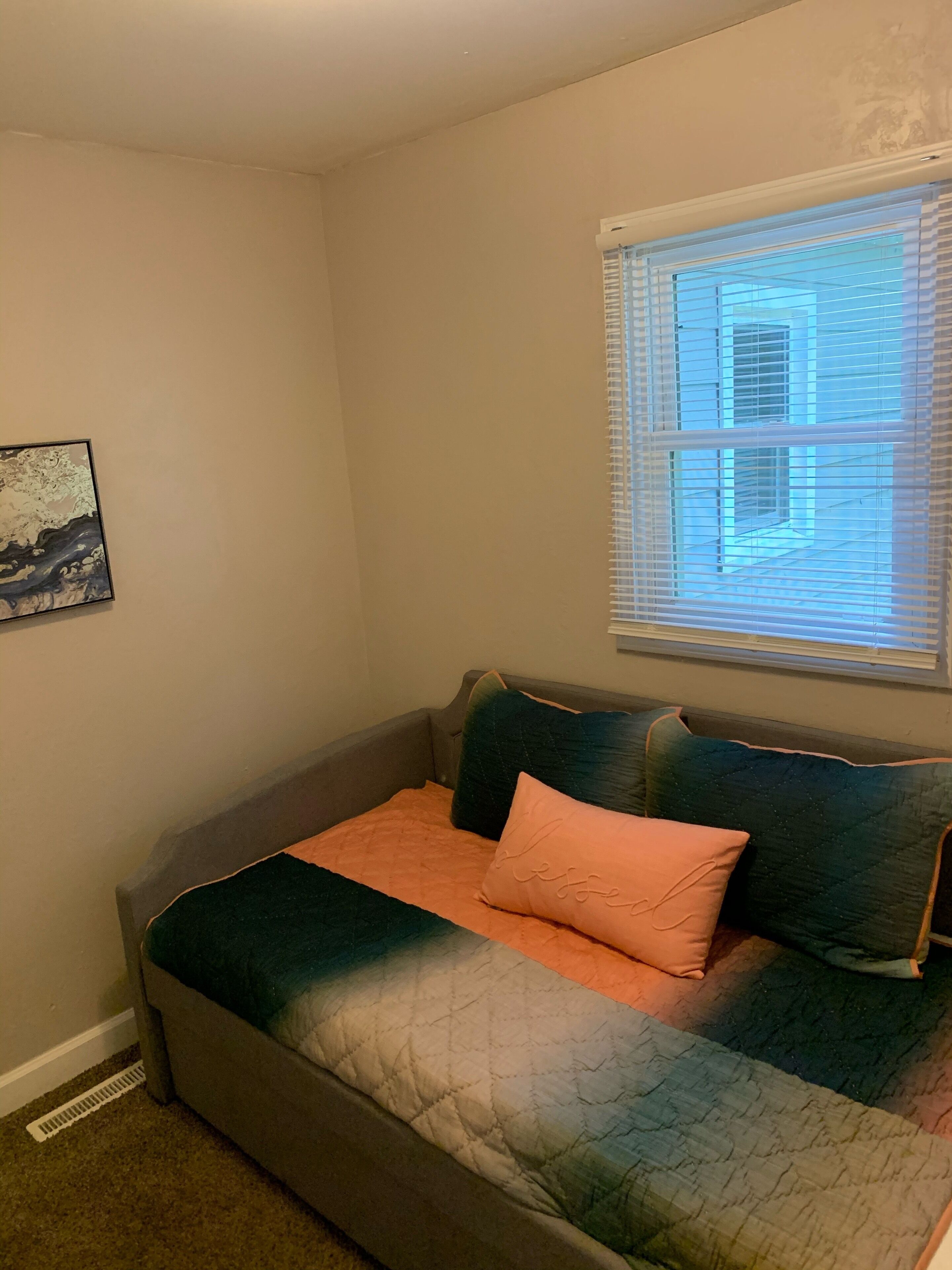 A bedroom with a bed, a window with blinds, a wall-mounted picture, and a radiator.