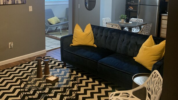 A modern living room with a dark blue sofa, yellow cushions, a glass coffee table, and a black and white patterned rug. - ~Chandler’s Chateau in the Heart of Brevard ~ (Brevard)