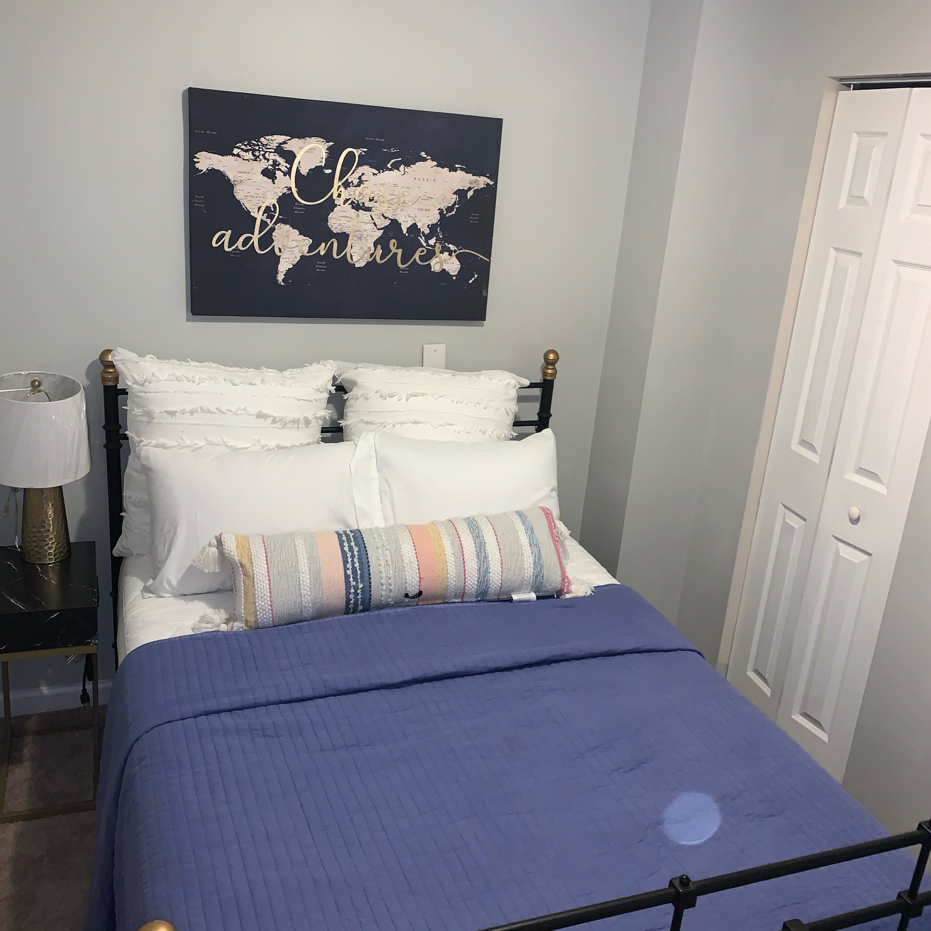 Un lit bien fait, avec une couverture bleue, des oreillers blancs et une carte du monde encadrée au-dessus.