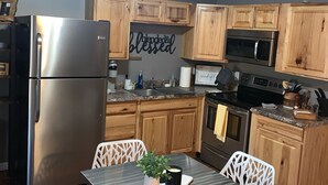 A kitchen with wooden cabinets, a stainless steel refrigerator, a microwave, and a stove. There is a table with chairs and a potted plant. - ~Chandler’s Chateau in the Heart of Brevard ~ (Brevard)