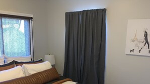 A neatly made bed with striped bedding, a window with sheer curtains, a wall-mounted lamp, and a painting of a figure with a dog. - ~Chandler’s Chateau in the Heart of Brevard ~ (Brevard)