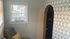 A room with a grey upholstered chair, a patterned rug, a window with blinds, and a wall with a geometric pattern. - ~Chandler’s Chateau in the Heart of Brevard ~ (Brevard)