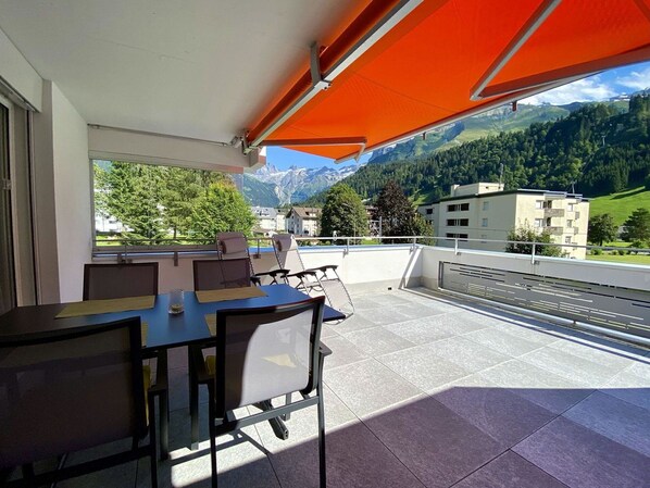 Eine Terrasse mit Tisch und Stühlen, Blick auf Berge und Gebäude im Hintergrund.