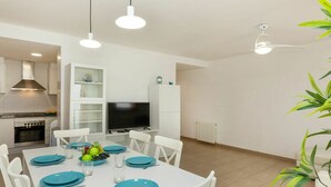 Une cuisine moderne avec des meubles blancs, un four encastré et un coin repas doté d’une table blanche, mise pour quatre personnes, avec des assiettes bleues.