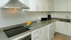 Une cuisine moderne avec des meubles blancs, une plaque de cuisson à induction noire, une machine à café et un grille-pain.