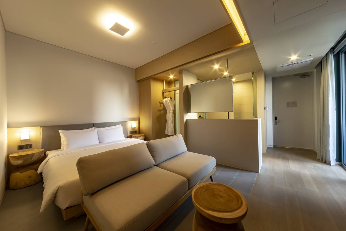A modern hotel room with a bed, sofa, bedside tables, and a large mirror.