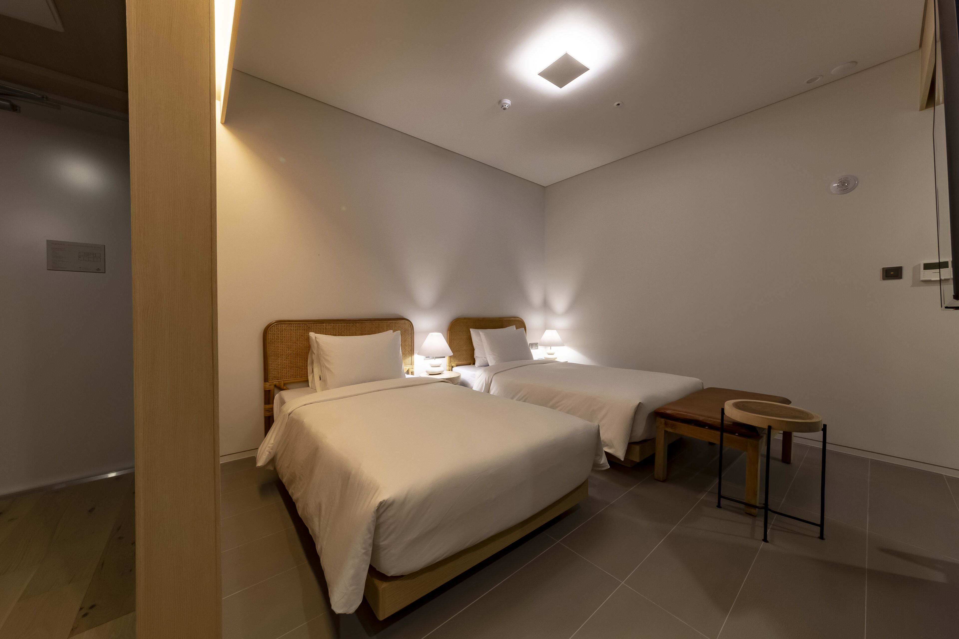 A hotel room with two single beds, a small table, and a bedside table with lamps.