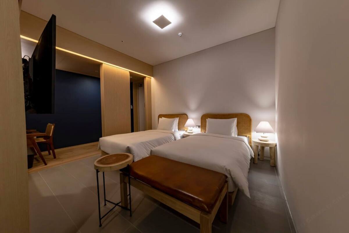 A hotel room with two beds, a bench, a small table, and a TV.