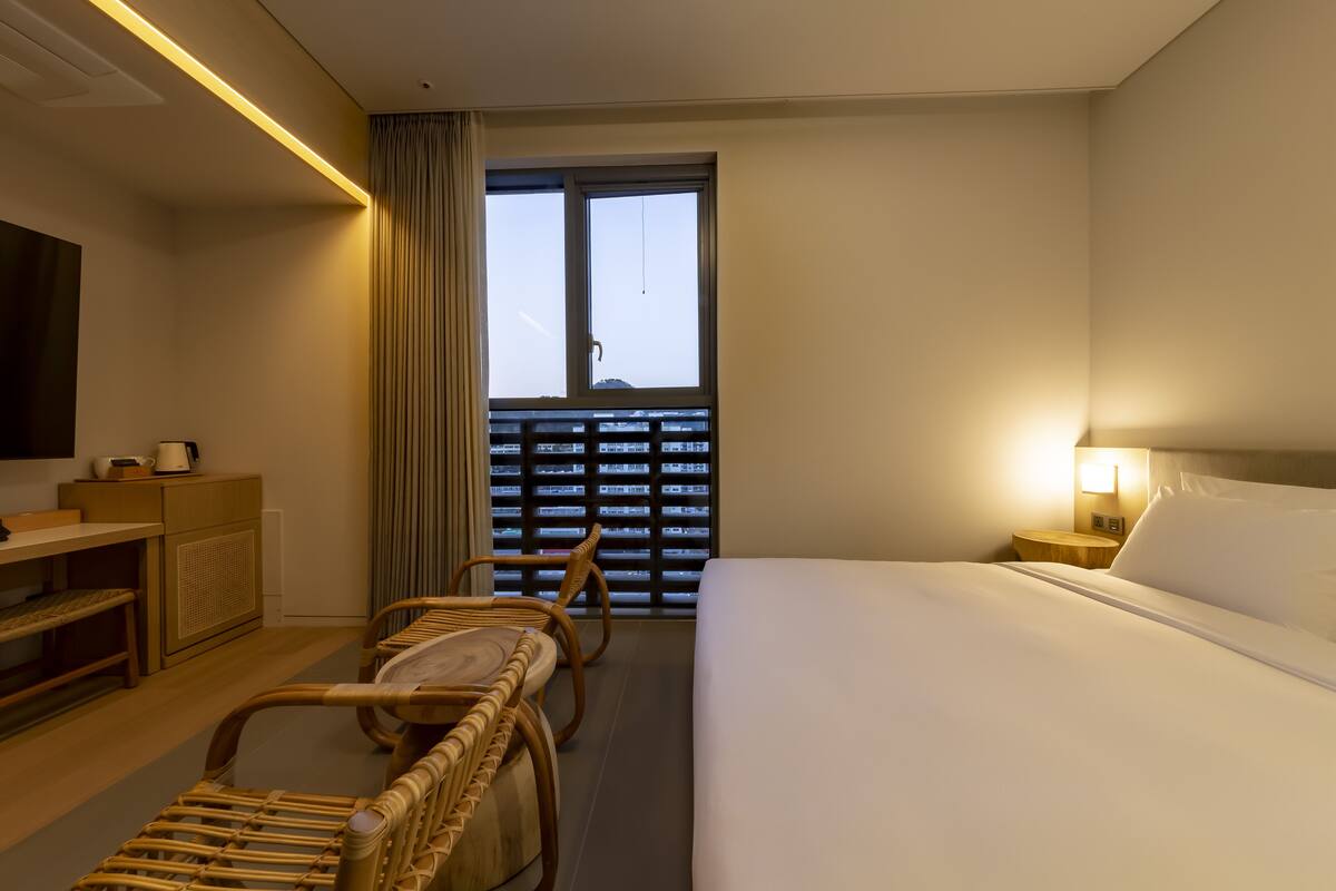 A hotel room with a bed, a desk, a chair, a TV, and a window with blinds.