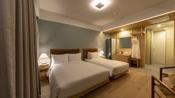 Habitación de hotel con dos camas, piso de madera, un espejo, un perchero para bata y una mesita con lámpara.
