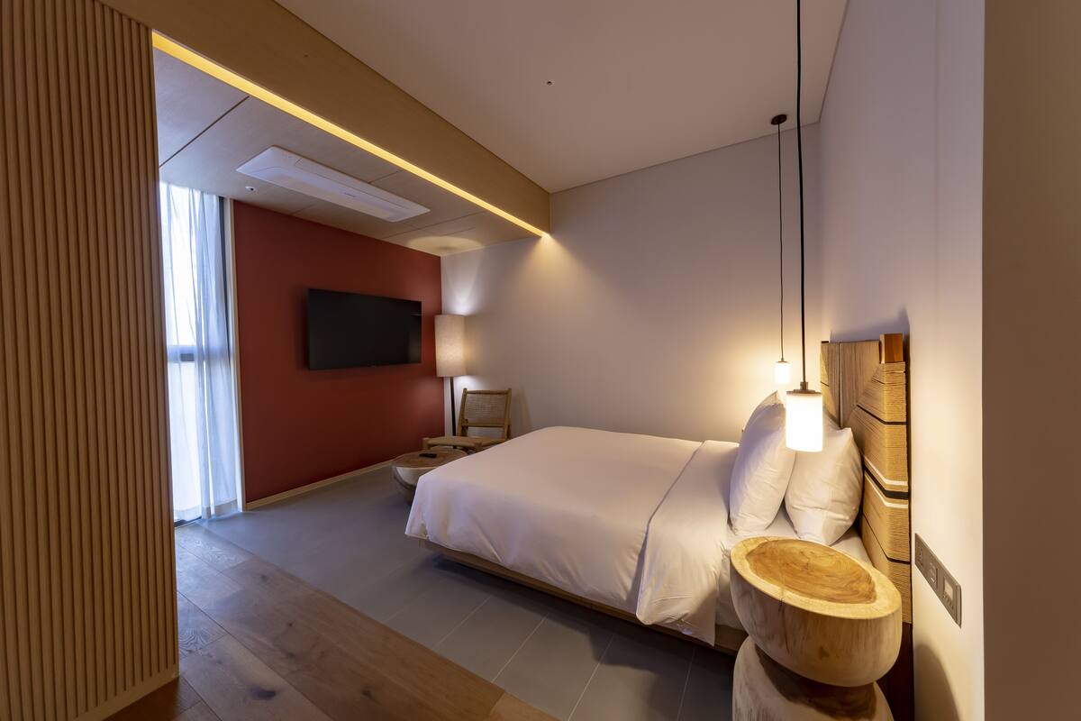 A modern bedroom with a large bed, bedside tables, a flat-screen TV, and a wooden accent piece.