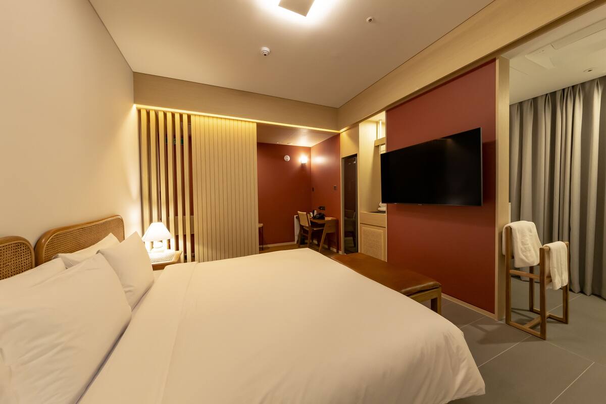 A hotel room with a large bed, a desk, a chair, a television, and a mirror.