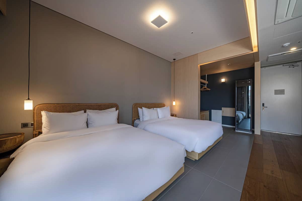 A modern hotel room with two large beds, a wooden headboard, a bedside table, and a wardrobe.