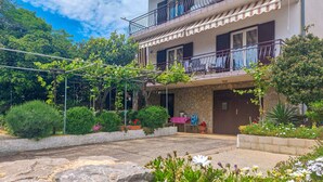 A two-story building with a balcony, surrounded by greenery and flowers. - Cosy apartment for 5 guests with WIFI, A/C, TV and terrace (Novi Vinodolski)