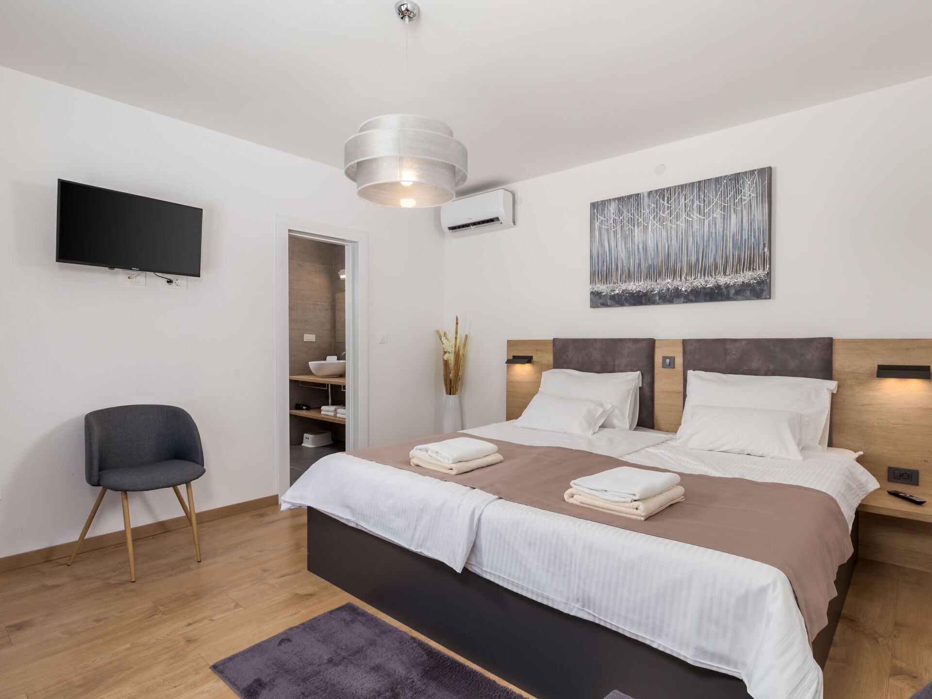 Une chambre moderne avec un grand lit, une télévision et une salle de bain visible à travers une porte ouverte.